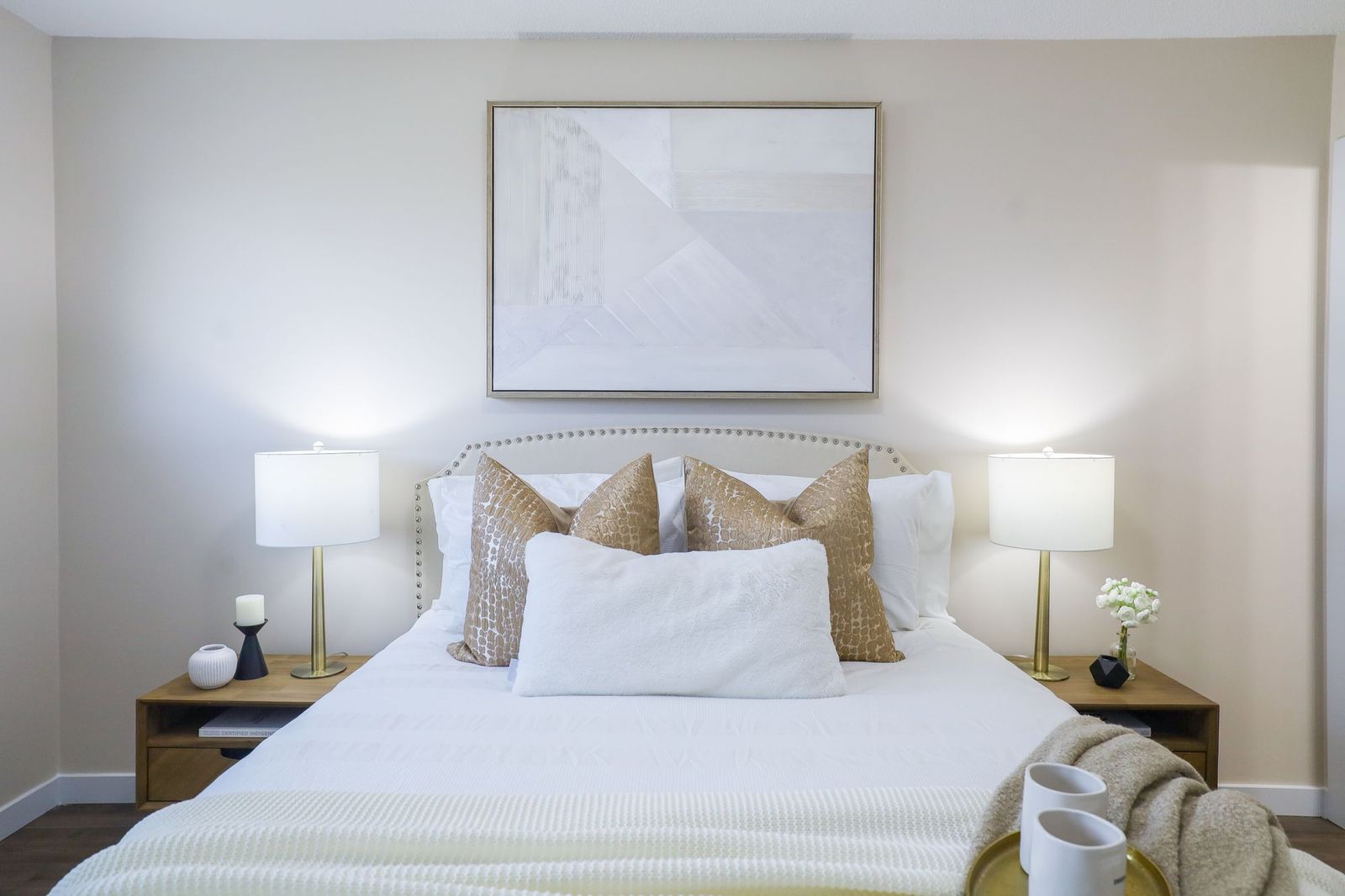 A styled bedroom in warm neutral tones with brass lamps and layered bedding